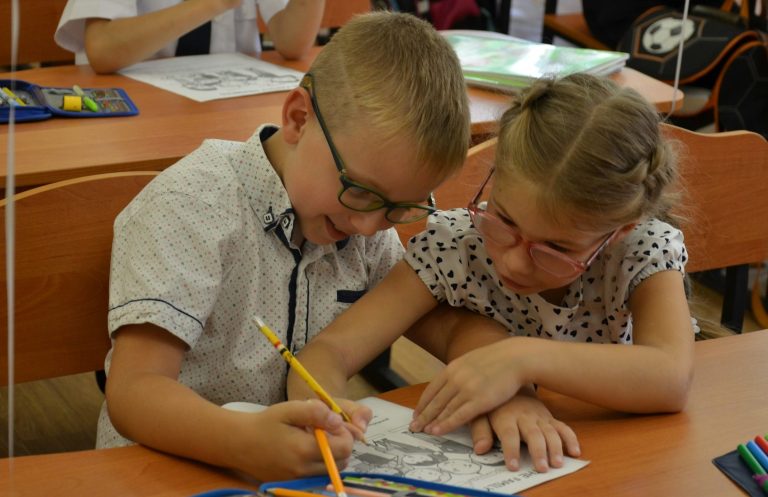 Ein Junge und ein Mädchen im Kindergartenalter malen gemeinsam in einem Heft.