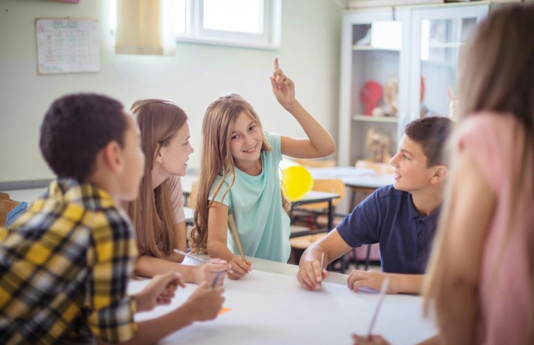 Vier Kinder sitzen an einem Tisch und bearbeiten gemeinsam eine Aufgabe.